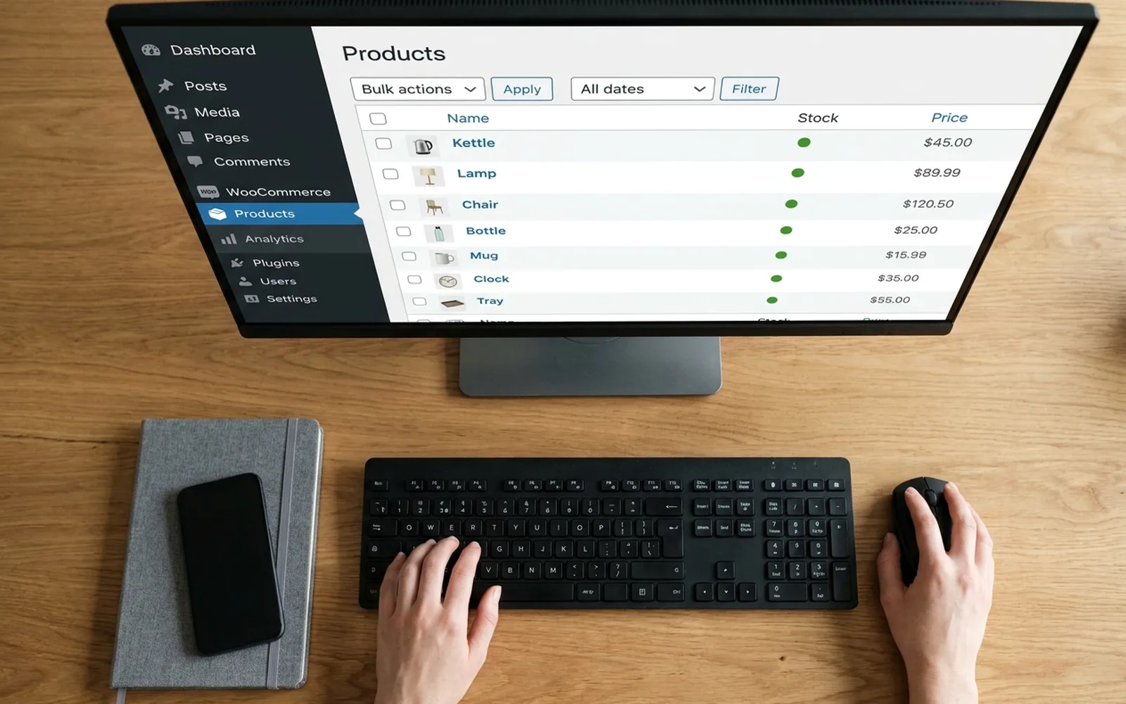 Overhead view of a person working at a desktop computer showing a WooCommerce product list in the WordPress admin.