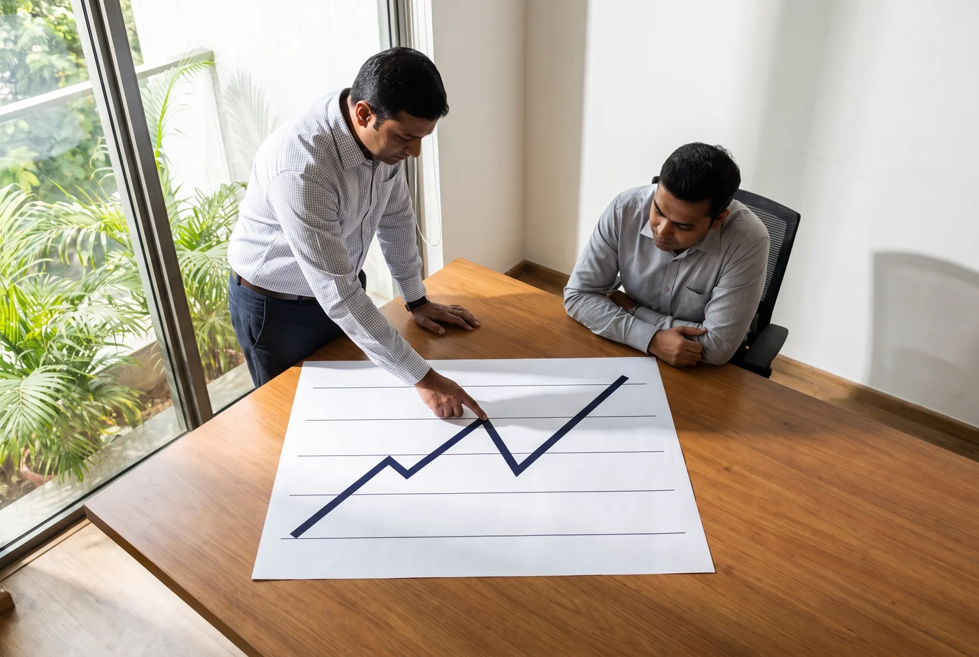 Two colleagues over a printed graph whose line drops sharply and then climbs back higher than it started, one tracing the drop.