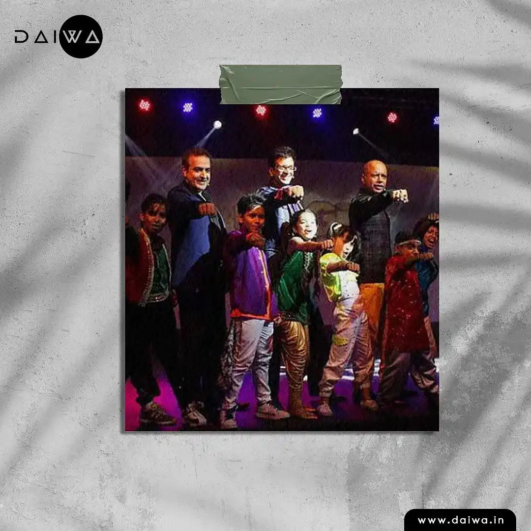 Taped-on photo of three men and several costumed children on a lit stage, all pointing fists toward the camera