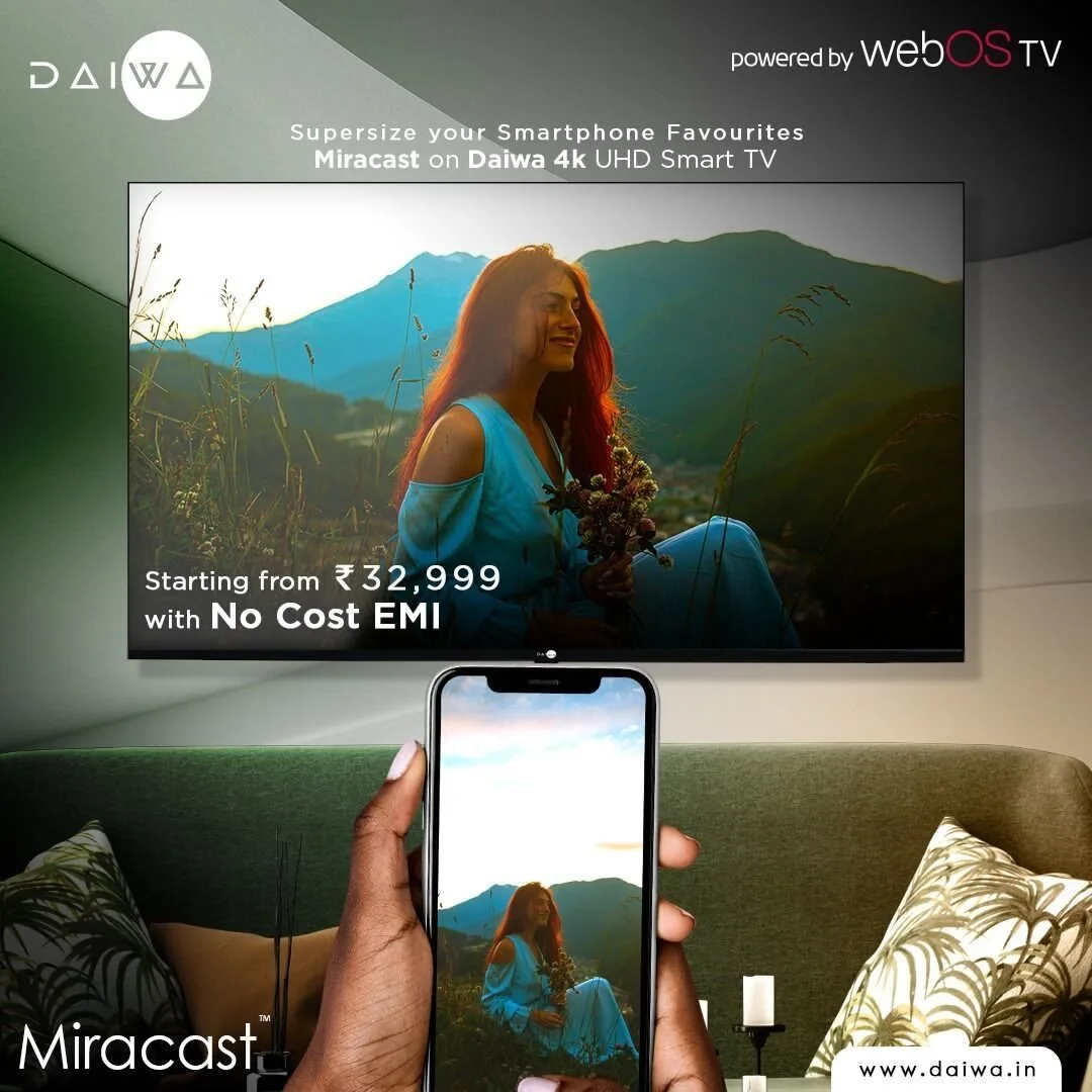 Hand holding a phone that mirrors a woman's mountain photo onto a wall-mounted TV; Miracast branding and a No Cost EMI offer