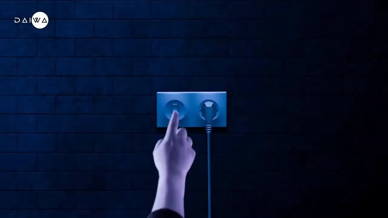 Finger presses the switch on a blue wall socket next to a plugged-in cable, against a dark blue brick wall