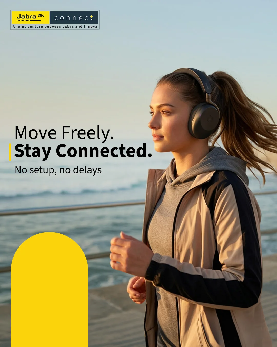 Woman jogging along a seaside promenade in over-ear headphones, headline Move Freely. Stay Connected.