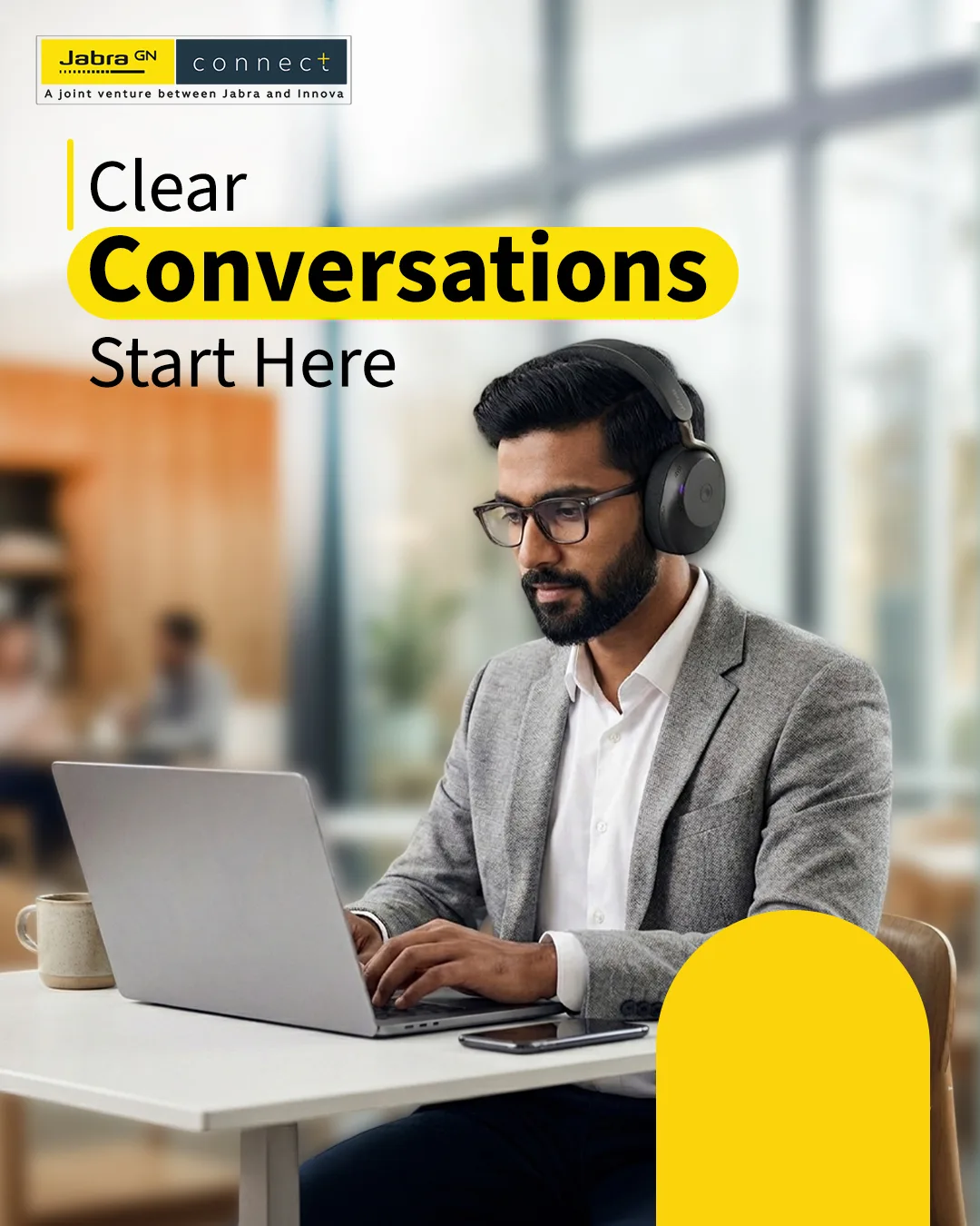 Man in a grey blazer typing on a laptop in a bright, window-lit space, wearing black headphones, headline Clear Conversations Start Here