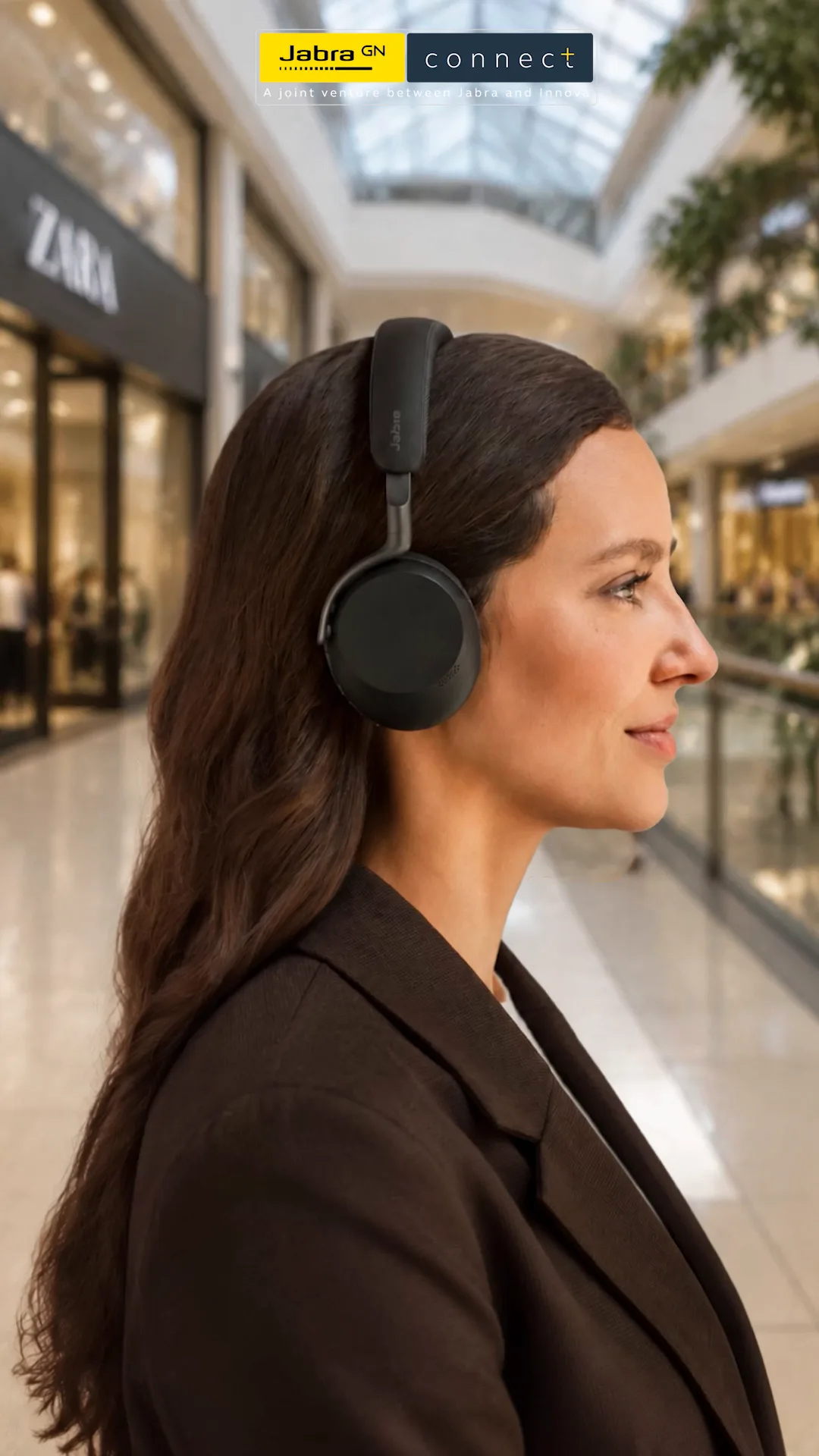 Woman in profile wearing black Jabra headphones in a bright shopping mall with a glass roof, Jabra Connect logo above