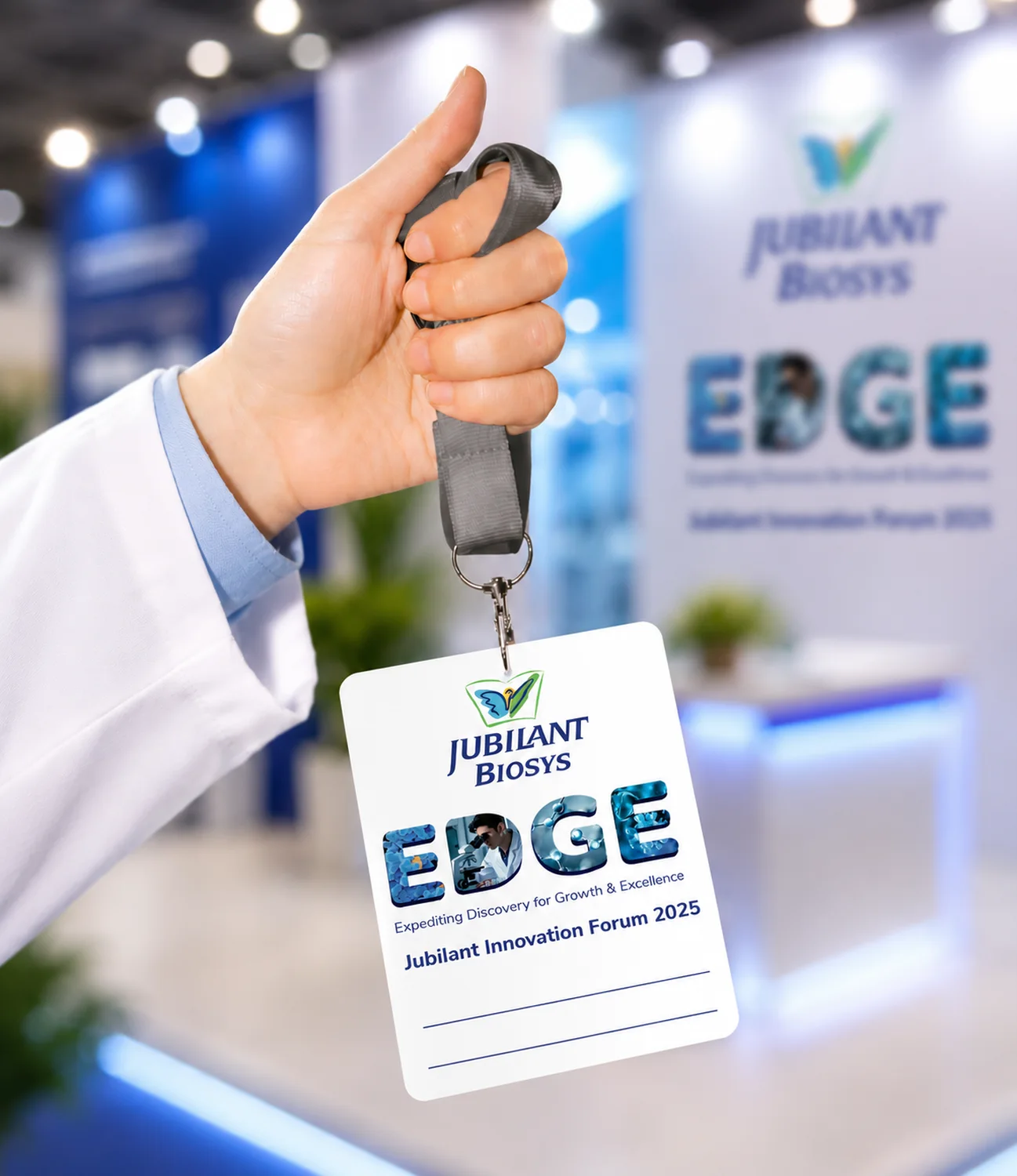 Jubilant Biosys EDGE delegate badge on a lanyard, held in front of the exhibition stand