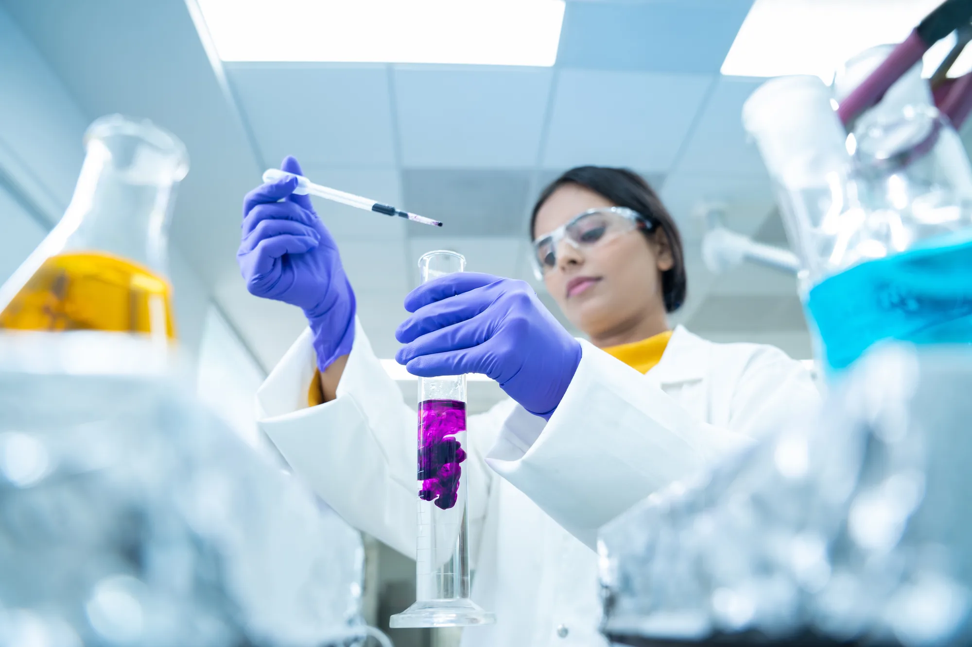 A Jubilant Biosys researcher pipetting a sample into a graduated cylinder in the laboratory